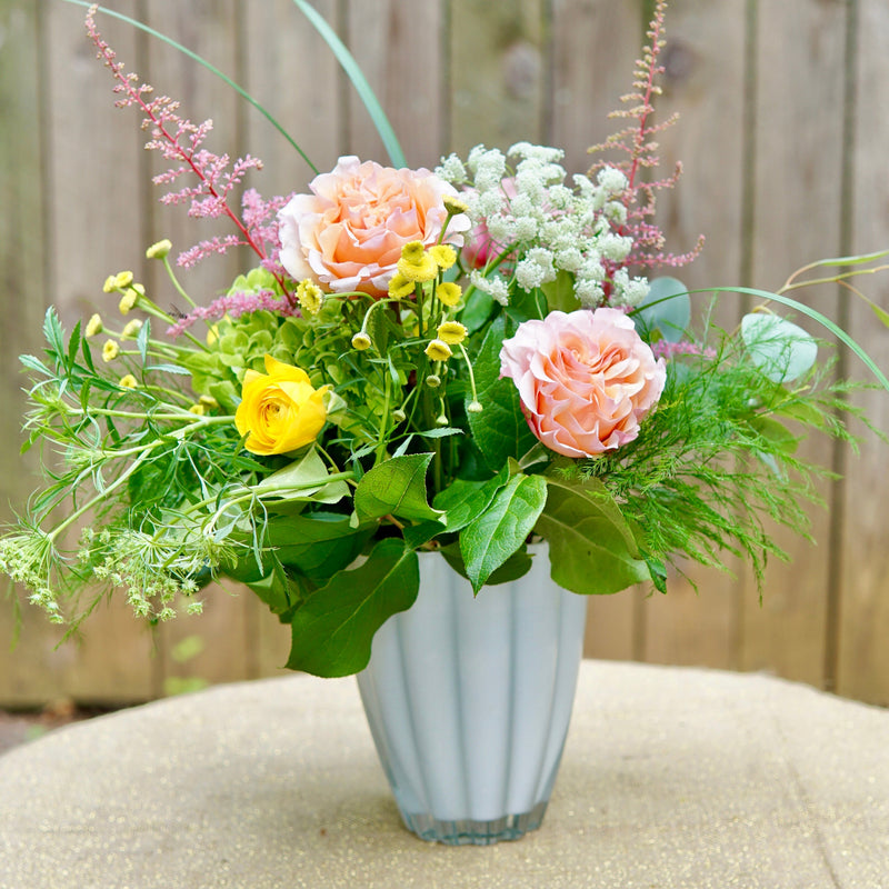 Floral arrangement in a white vase on a wooden surface with a wooden fence background