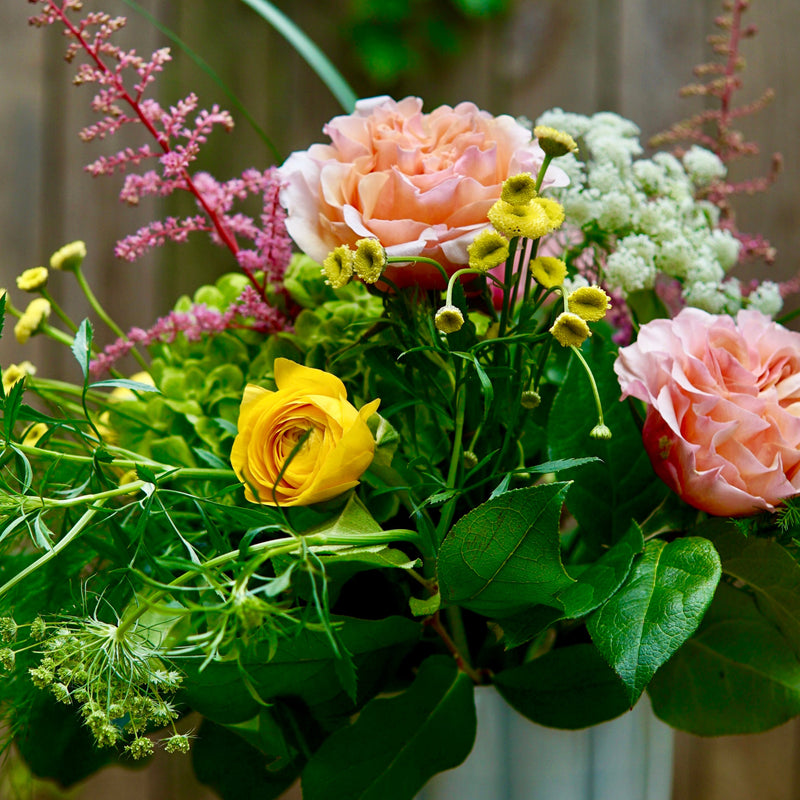 Bouquet of flowers with greenery in a vase against a wooden background