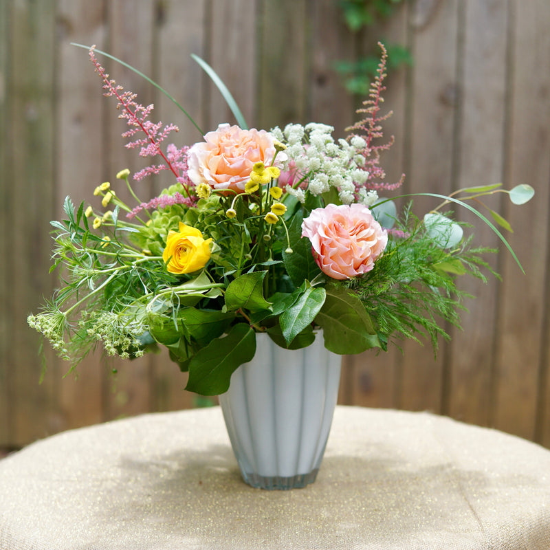 Floral arrangement in a white vase on a table with a wooden background