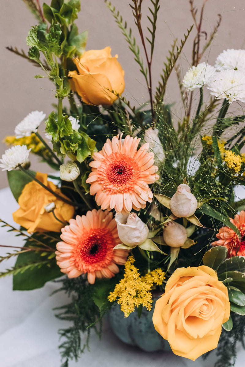 A vibrant medley of buttery yellow, rich peach, and crisp white blossoms bursts with life in a charming scalloped vase. Named for a quaint south Georgia town renowned for its Old South Day food, arts and crafts festival.