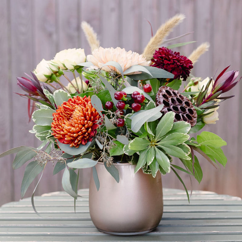 Floral arrangement with red, orange, and green flowers in a vase on a wooden surface.
