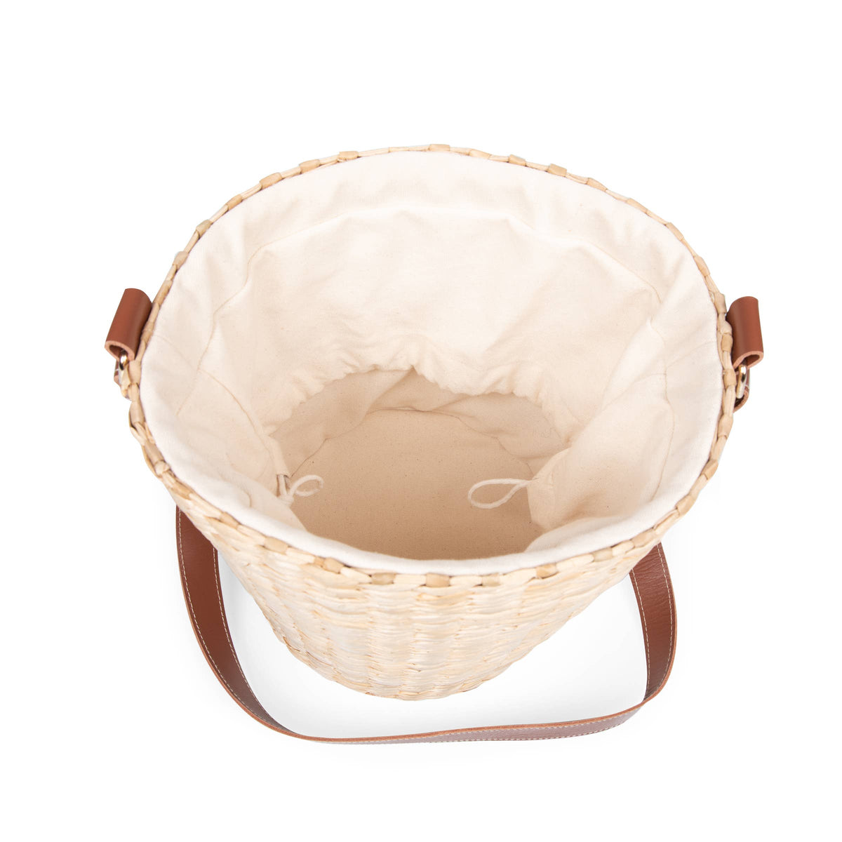 Beige handwoven rush bucket tote with cream lining and brown leather handles, viewed from above with open top.