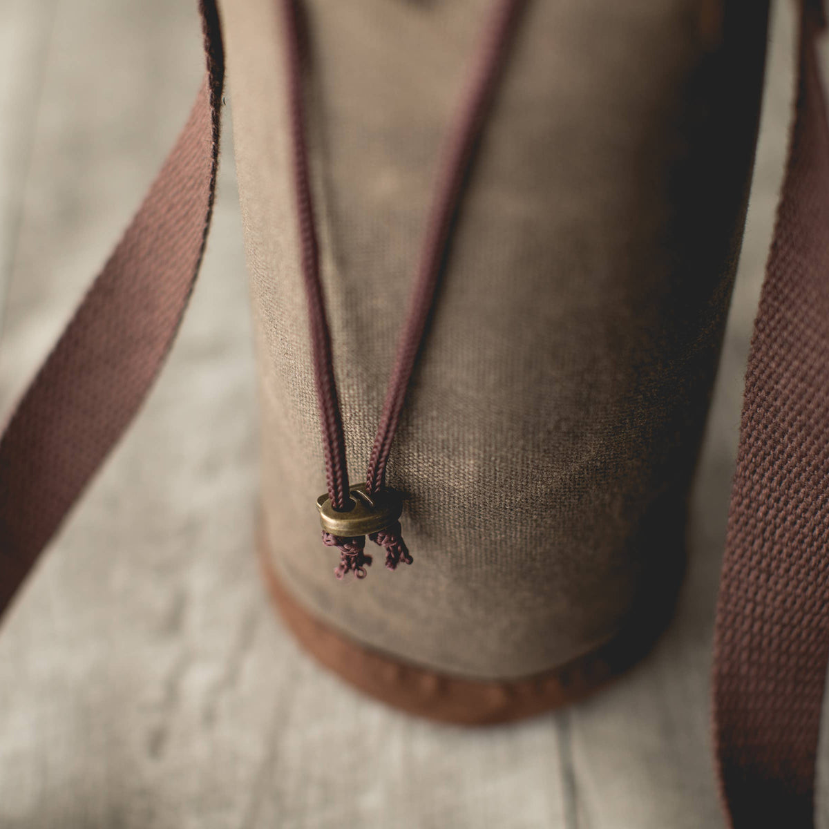 Distressed waxed canvas wine tote with burgundy handles and brass drawstring closure detail
