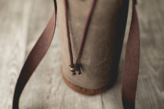 Distressed waxed canvas wine tote with burgundy handles and brass drawstring closure detail