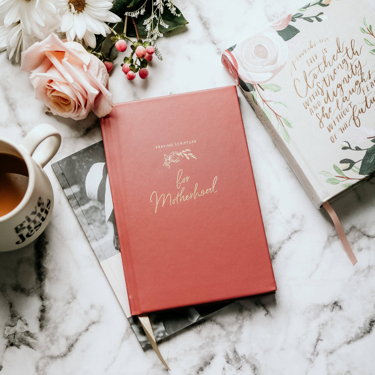 Coral prayer journal "for Motherhood" surrounded by peach roses, white daisies, coffee cup, and botanical notecards on marble