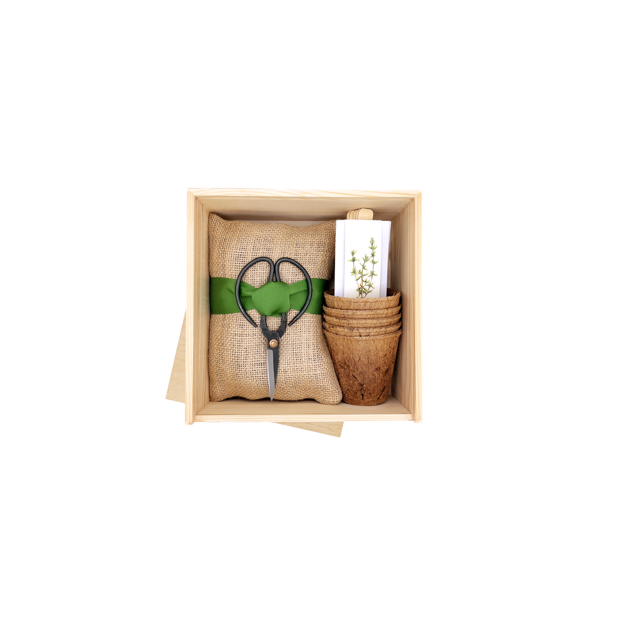 Open wooden garden box containing burlap pouch tied with green ribbon and black plant scissors, beside woven basket with plant care booklet and paper