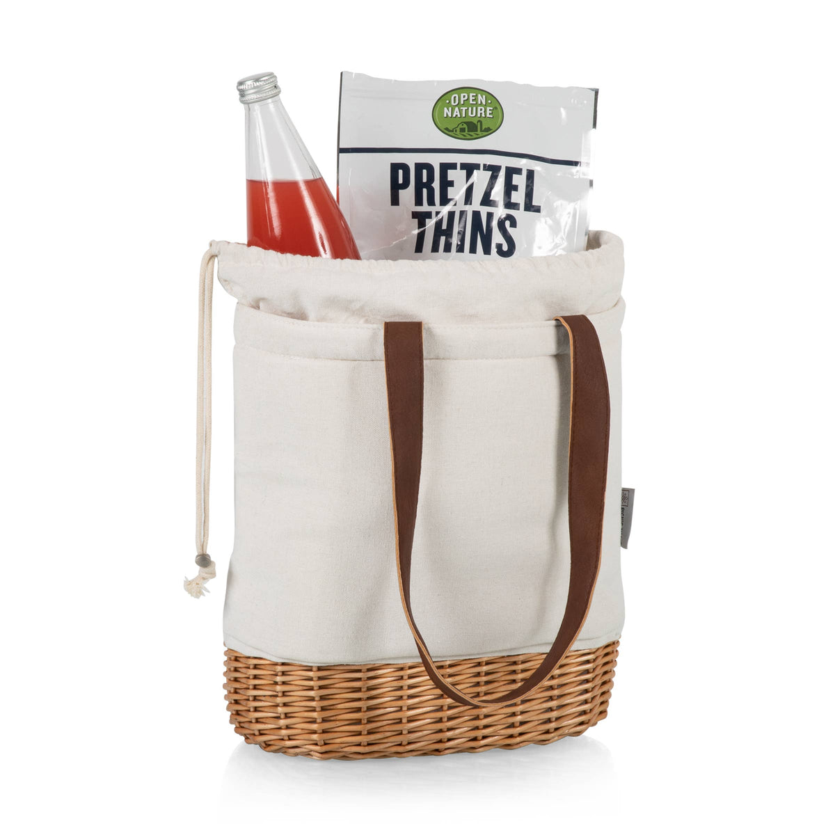 Pico insulated tote with cream canvas body, brown leather handles, and natural wicker base, holding a beverage bottle and pretzel bag