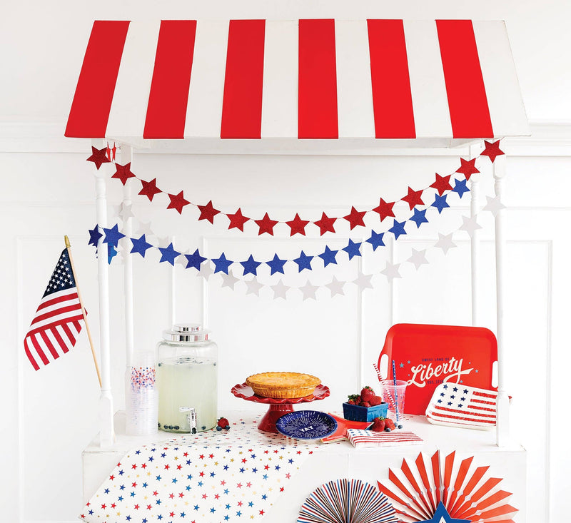 Glitter star banners in red and blue arranged as curved garlands with patriotic 4th of July party styling and red-white striped canopy