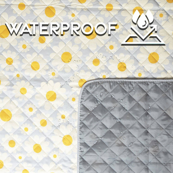 White quilted picnic blanket with yellow daisy print and waterproof gray backing, folded to show both sides with water droplets