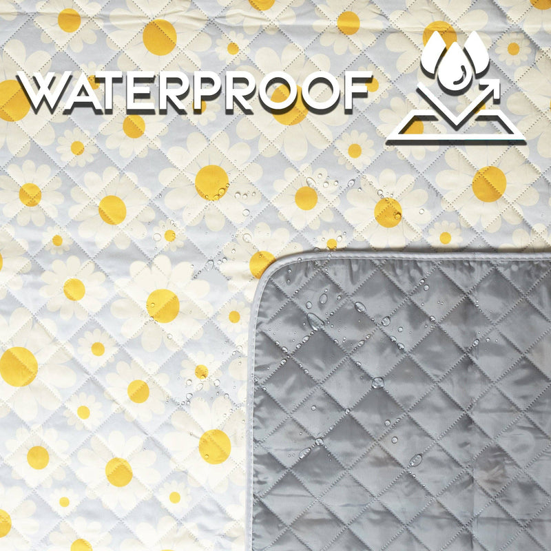White quilted picnic blanket with yellow daisy print and waterproof gray backing, folded to show both sides with water droplets