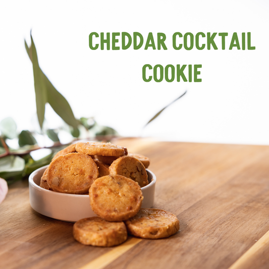 Golden cheddar cocktail cookies in white bowl on wooden surface with fresh eucalyptus sprigs