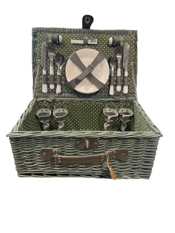 Open woven wicker picnic basket with polka-dot green interior, showing complete service set for four with plates, glasses, cutlery, and accessories