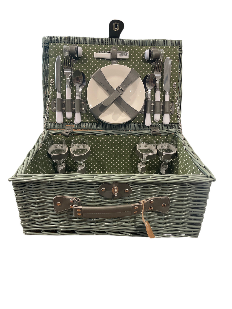 Open woven wicker picnic basket with polka-dot green interior, showing complete service set for four with plates, glasses, cutlery, and accessories