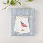 White mini notecard with illustrated American flag, gold pole, and grass, on striped envelope with twine and greenery
