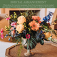 Mixed floral arrangement with peach roses, coral gerbera daisies, pink carnations, blue delphinium, thistle, and green hypericum berries in a clear glass vase