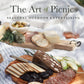 "The Art of Picnics" cookbook cover with author Alanna O'Neill, featuring styled charcuterie boards with bread, cured meats, cheese, and fresh herbs
