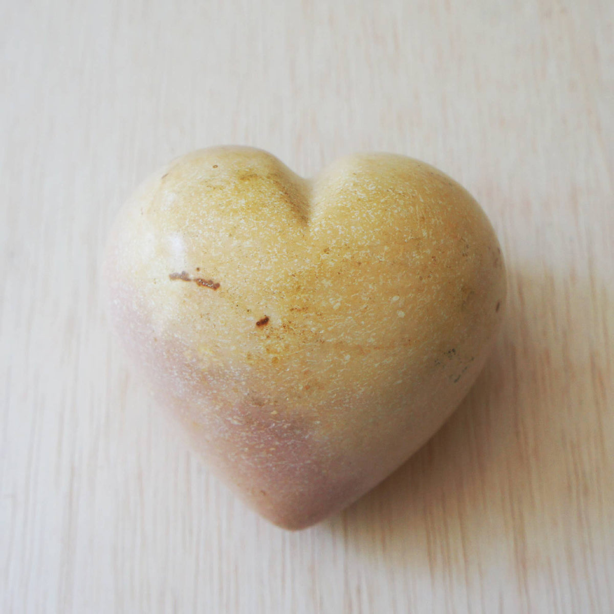 Polished cream soapstone heart with natural color variations and hand-carved texture, displayed on light wood.