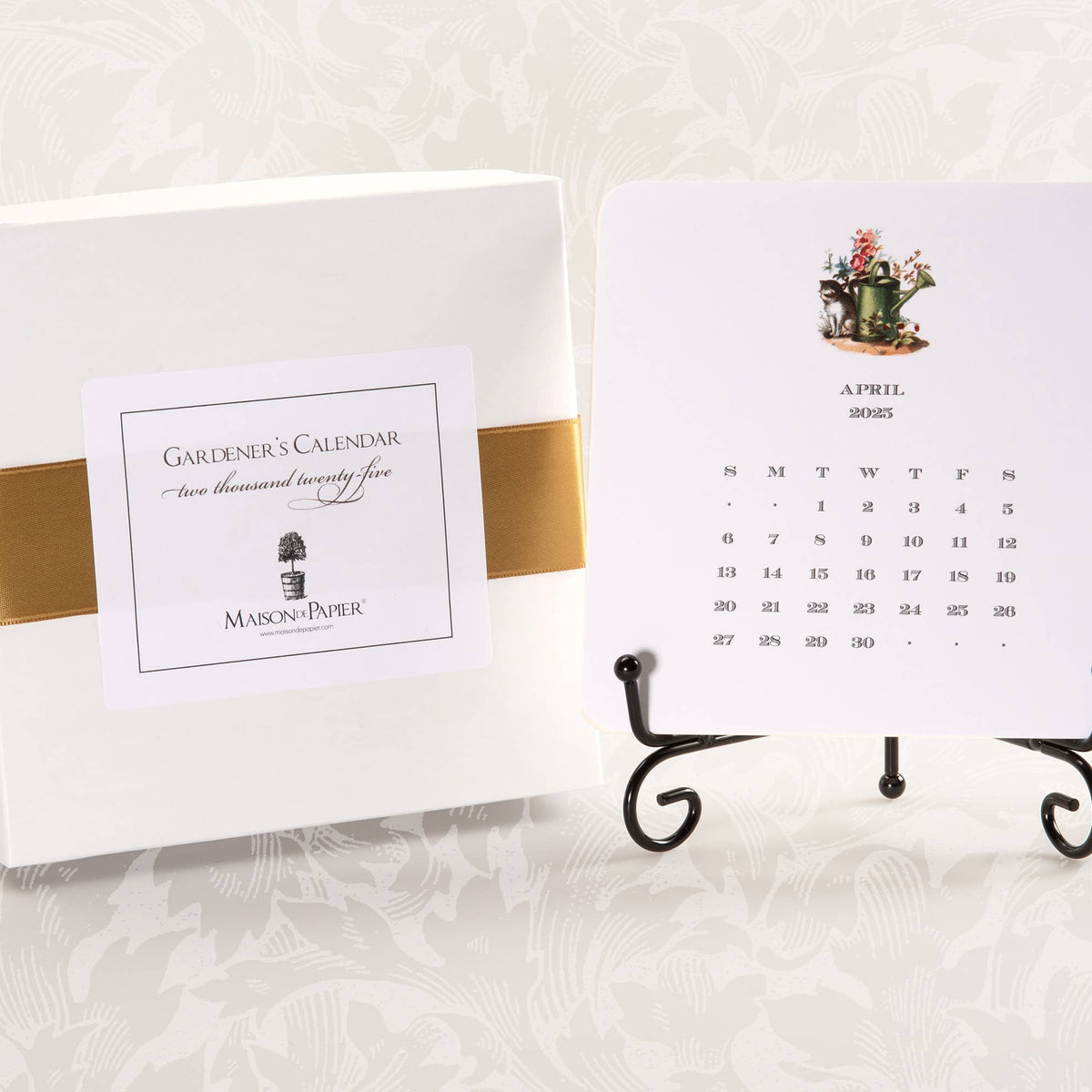 Gardener's Calendar box with white cardstock and gold foil band, displayed with April month card on black metal easel showing watering can illustration