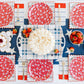 Flatlay of patriotic table with navy star tablecloth, red floral napkins, white place settings, and small bowls of berries and crackers