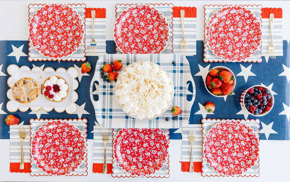 Flatlay of patriotic table with navy star tablecloth, red floral napkins, white place settings, and small bowls of berries and crackers