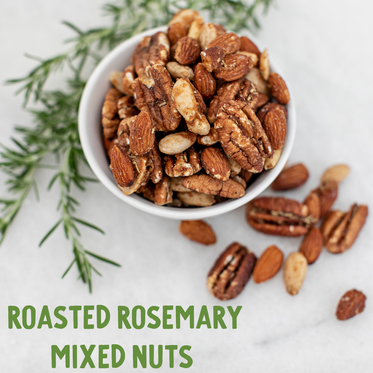 White bowl filled with roasted rosemary mixed nuts including almonds, pecans, and peanuts with scattered nuts and fresh rosemary sprigs