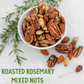 White bowl filled with roasted rosemary mixed nuts including almonds, pecans, and peanuts with scattered nuts and fresh rosemary sprigs