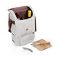 Cream canvas wine tote with brown accents, open to reveal red and yellow wine bottles, wooden cutting board, cheese knives, and metal corkscrew displayed in front.