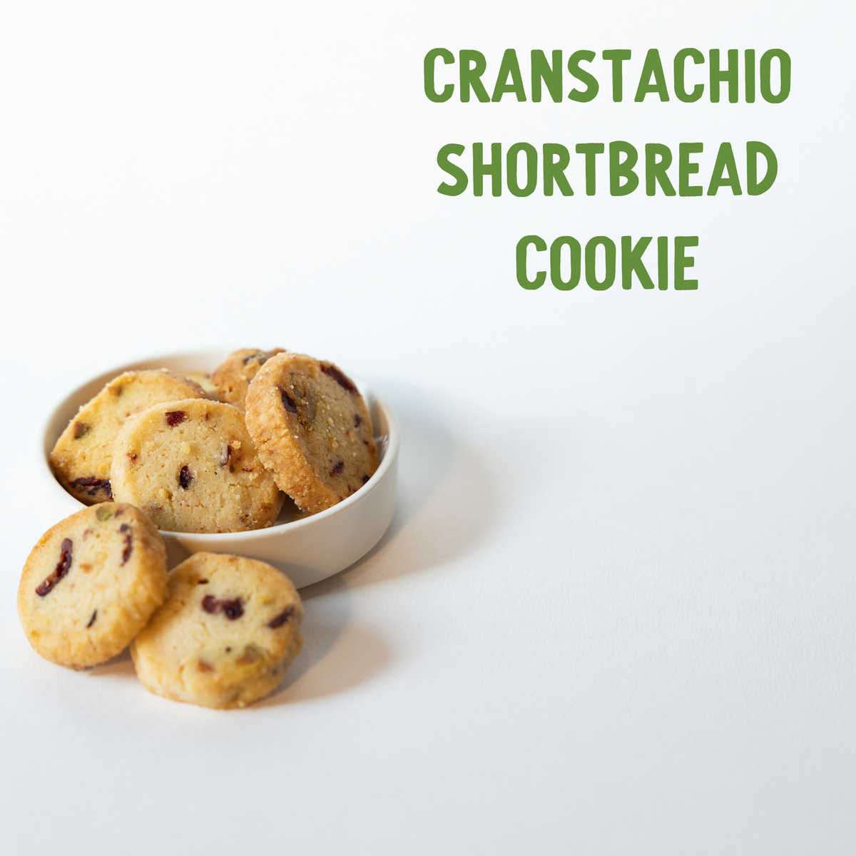 Buttery shortbread cookies studded with tart cranberries, spilling from a white ceramic bowl on a neutral background.