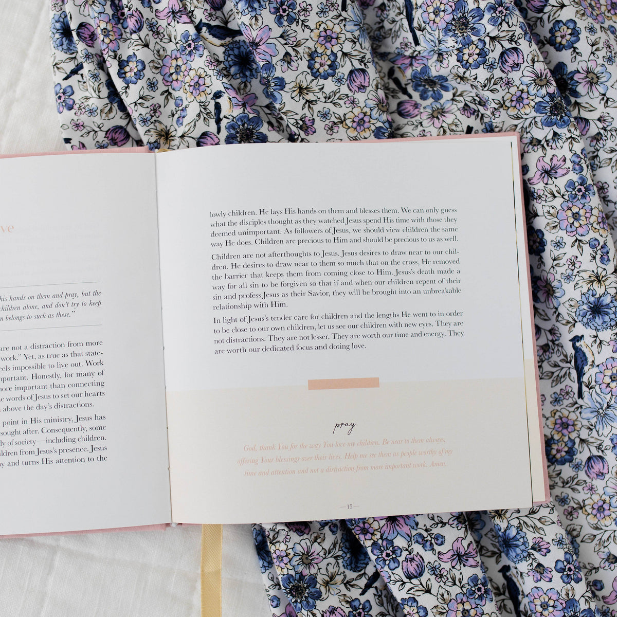Open motherhood devotional book with text pages displayed, resting on blue and purple floral patterned fabric