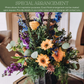 Colorful mixed floral arrangement with orange gerbera daisies, purple stock, blue delphinium, yellow roses, and eucalyptus greens in a clear vase.