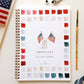 Spiral-bound Americana watercolor workbook with flag illustrations, surrounded by color swatches in reds, pinks, creams, and teals