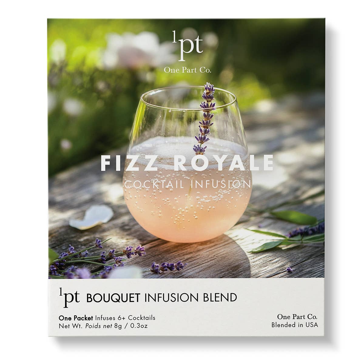 Peachy-pink sparkling Fizz Royale cocktail in a glass, garnished with fresh purple lavender, surrounded by lavender flowers on weathered wood