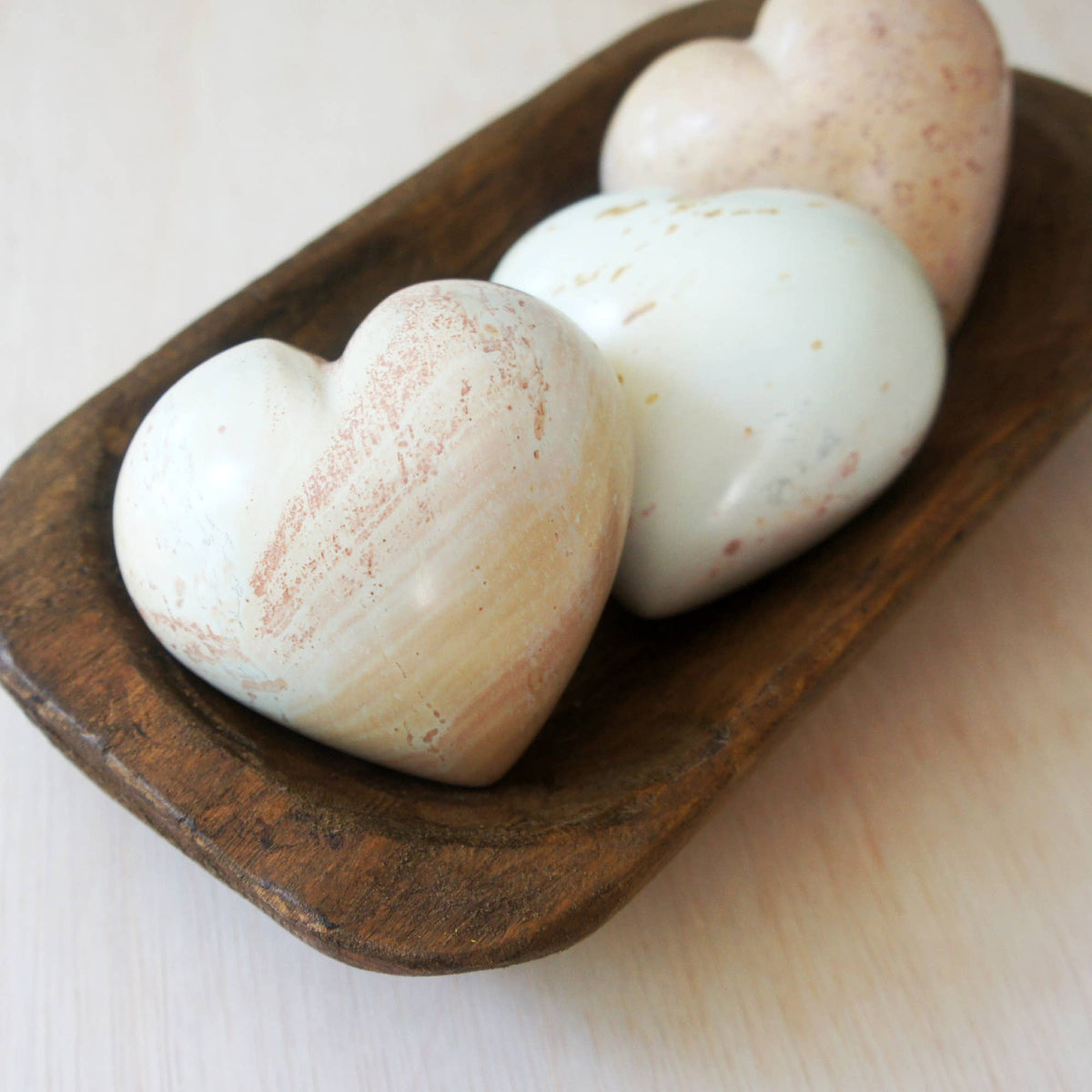 Handcrafted soapstone hearts with cream and rust-speckled finish, nested in dark wood bowl