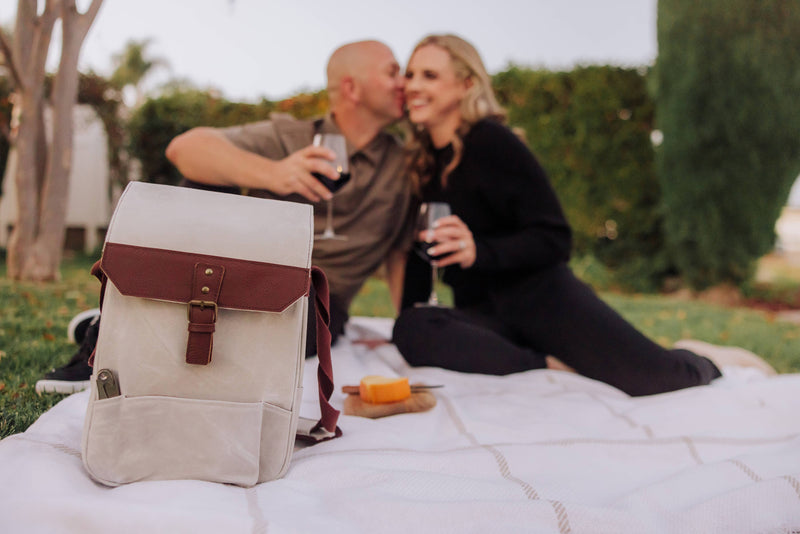 Cream insulated wine tote with burgundy leather flap, displayed on grass during outdoor picnic