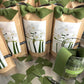 Kraft paper bags of paperwhite bulbs with green fabric ties, featuring white flower illustrations and green stems on labels.