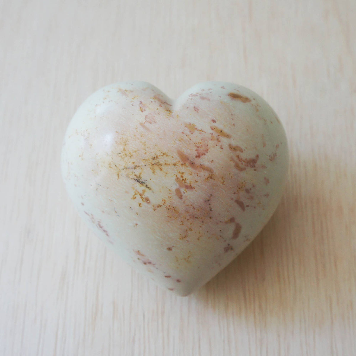 Polished soapstone heart with cream base and rose-gold natural stone markings on light wood surface.