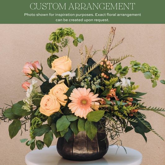 Blush and cream roses with pink gerbera daisy in dark ceramic vase, mixed with green foliage and delicate branches