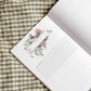 Open gardening journal with botanical flower and plant illustrations on cream pages and lined writing space, displayed on green gingham fabric.