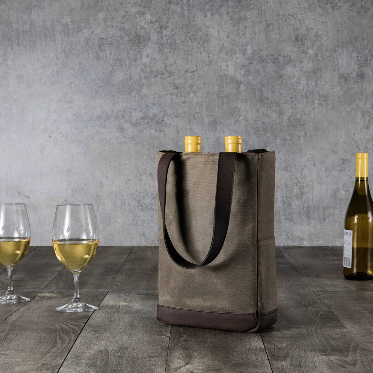 Tan and brown insulated wine tote with black handles holding two bottles, displayed with filled wine glasses and additional bottles on wooden surface