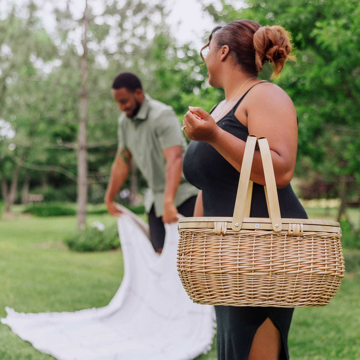 Beige handwoven wicker picnic basket with rope handles carried during outdoor park picnic