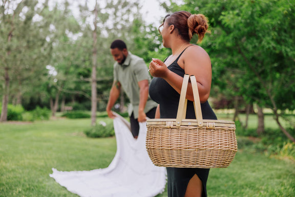 Beige handwoven wicker picnic basket with rope handles carried during outdoor park picnic