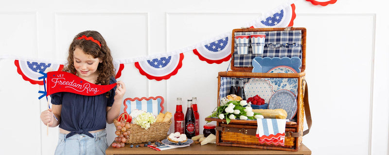 Child holding red "Let Freedom Ring" felt banner surrounded by red, white, and blue patriotic pennant bunting
