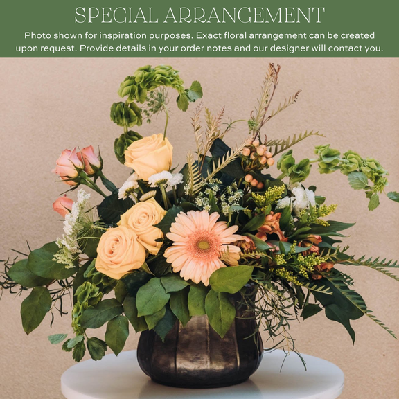 Peach roses and pink gerbera daisies with mixed greenery and ferns in a black rounded vase on neutral background.