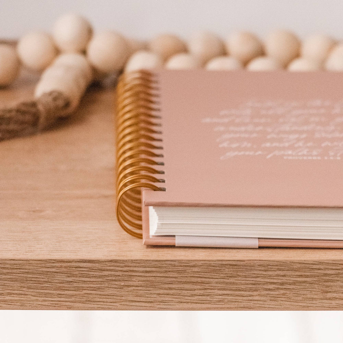 Beige hardcover spiral journal with gold binding and embossed text detail on wooden surface