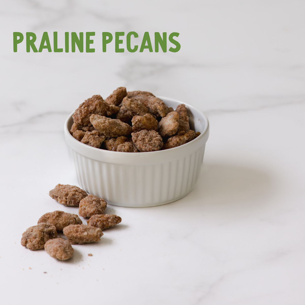 Praline pecans in white ceramic bowl with scattered nuts on marble surface