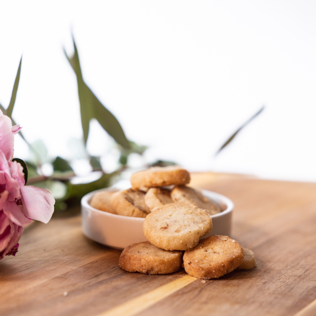 Pecan shortbread cookies in a white ceramic bowl on natural wood surface with fresh pink flowers
