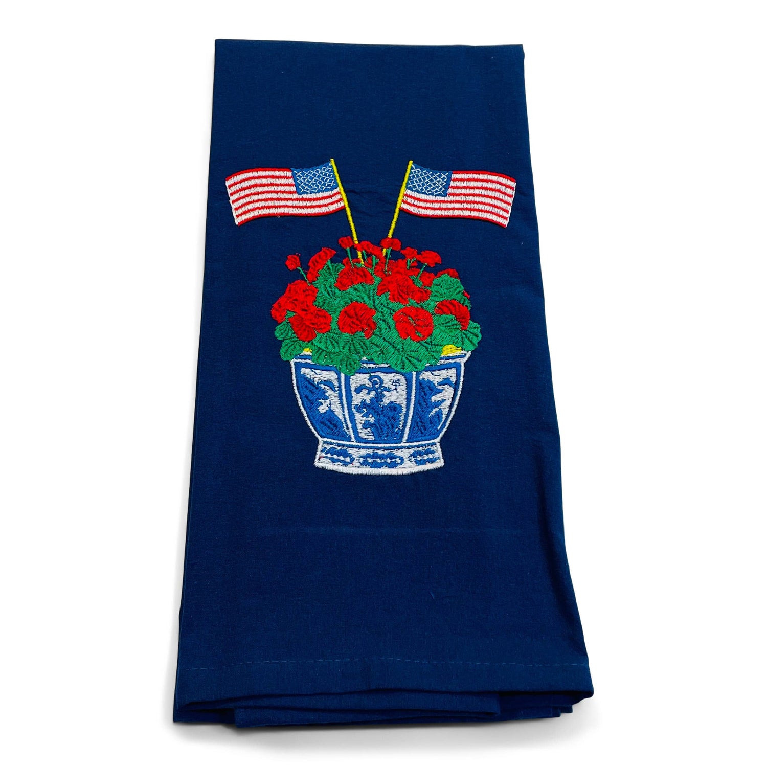 Navy cotton dish towel with embroidered American flags flanking red geraniums in a blue and white decorative pot.