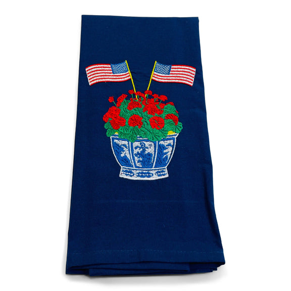 Navy cotton dish towel with embroidered American flags flanking red geraniums in a blue and white decorative pot.
