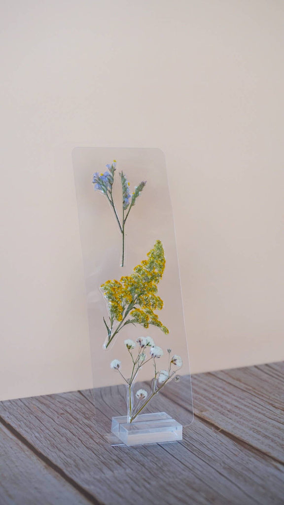 Pressed flower bookmark with blue forget-me-nots, yellow yarrow, and pale blue baby's breath on clear acrylic stand.