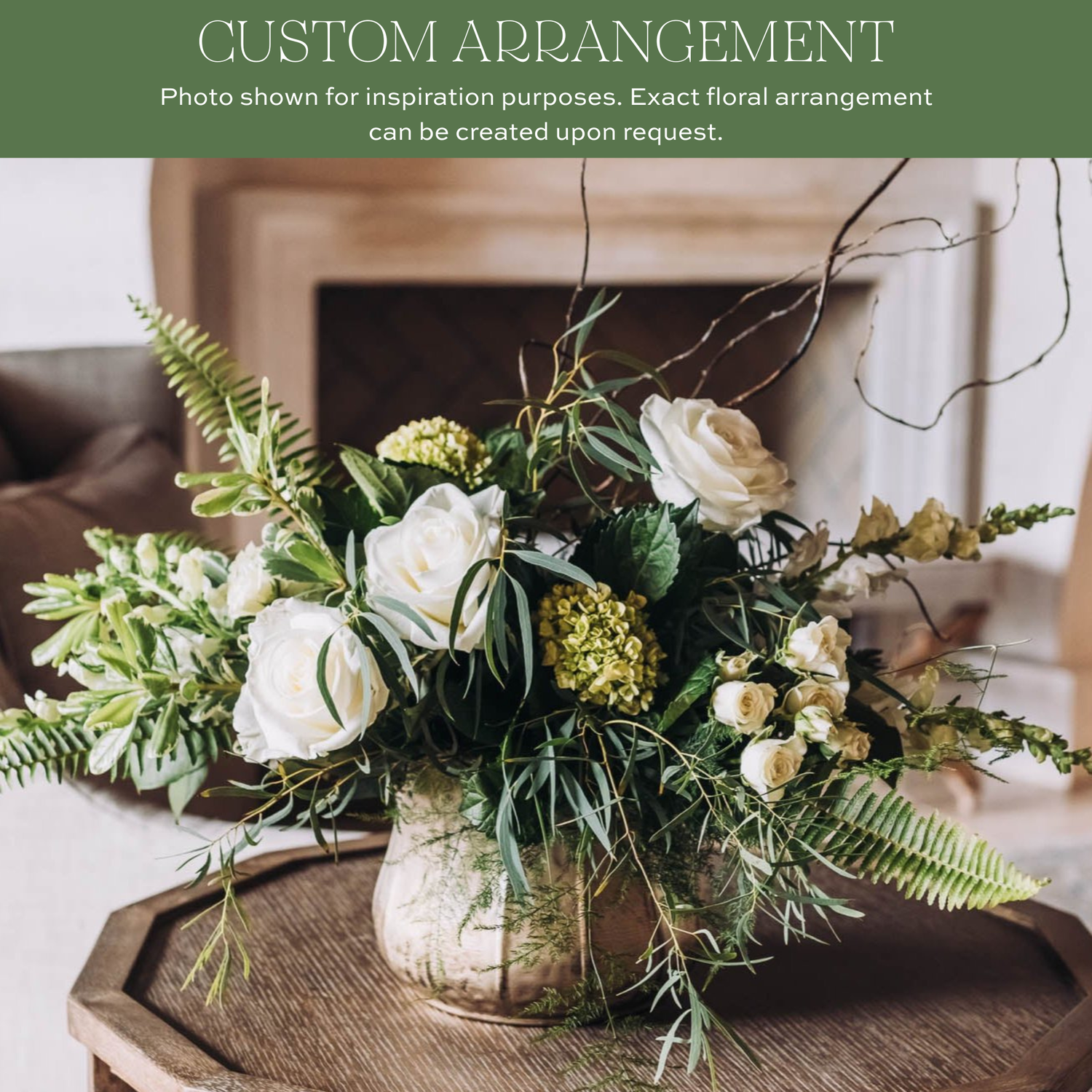 White roses with yellow cluster flowers, curling branches, and fern foliage in a clear glass vase on a wooden surface